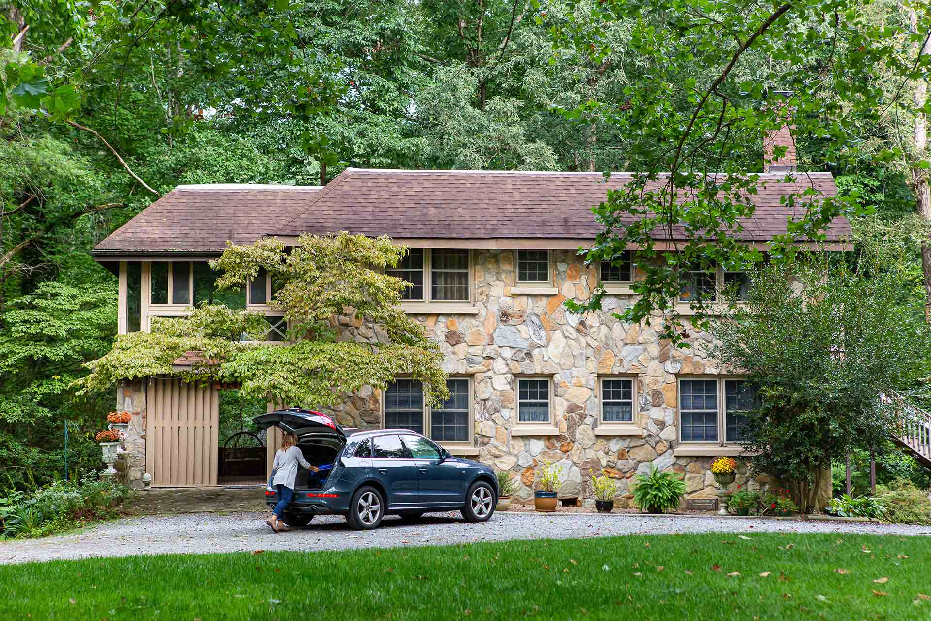 A woman puts things into the trunk of her SUV in front of an old stone house