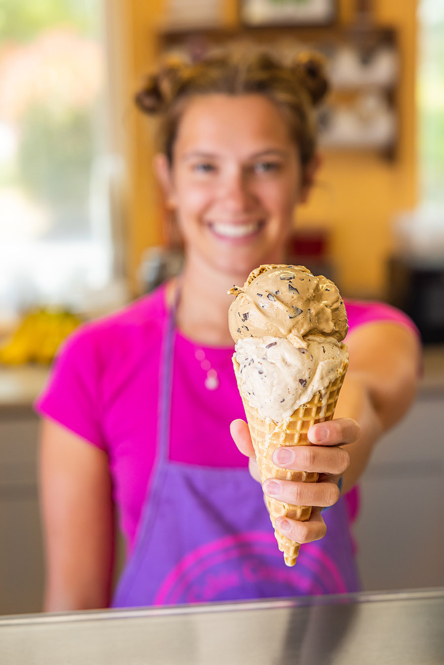 Celtic Creamery - CREDIT Tim Robison teenage girl wearing an apron holding out ice cream cone with 2 scoops toward the camea