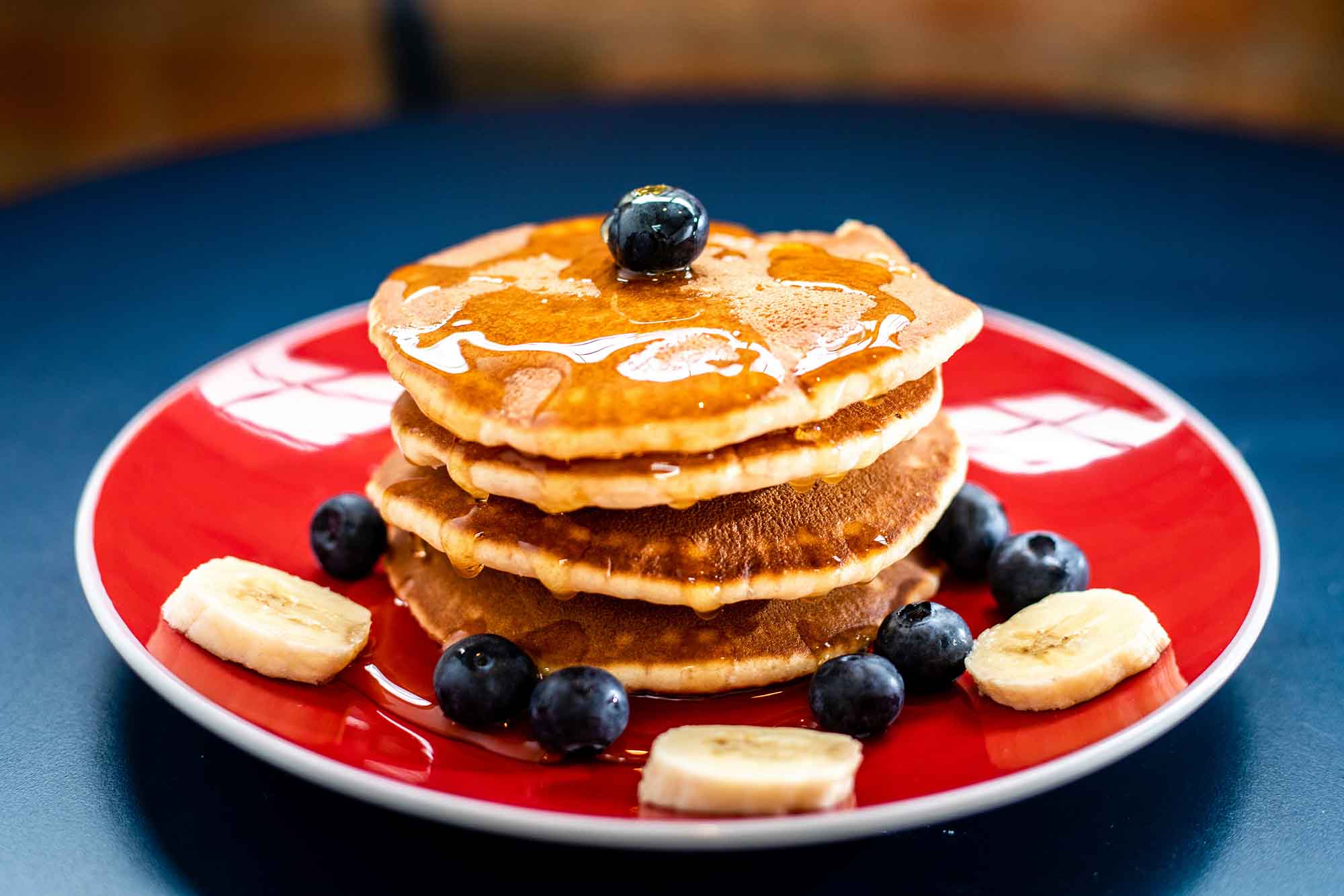 pancake breakfast sitting on a red plate with blueberries and bananas