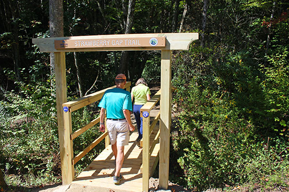 strawberry-gap-trail people crossing bridge at the start of a hiking trail through the woods